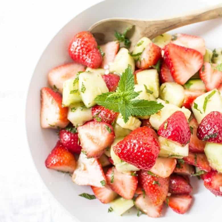 This is a picture of a cucumber salad with fresh mint and strawberries.