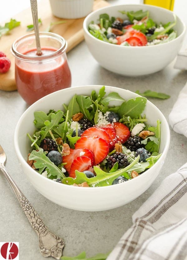This is a picture of a arugula salad topped with blackberries, strawberries and blue cheese.