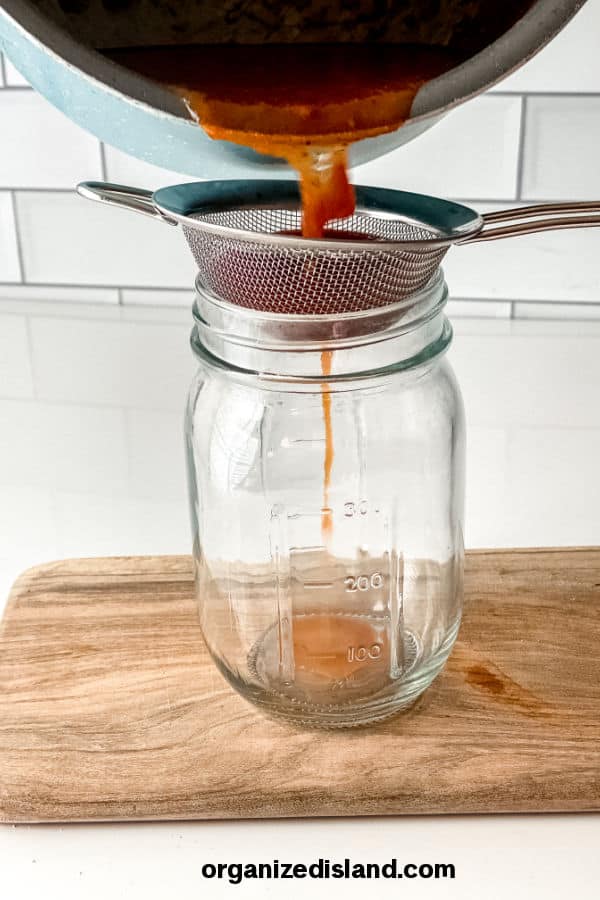 straining tomatoes in a jar