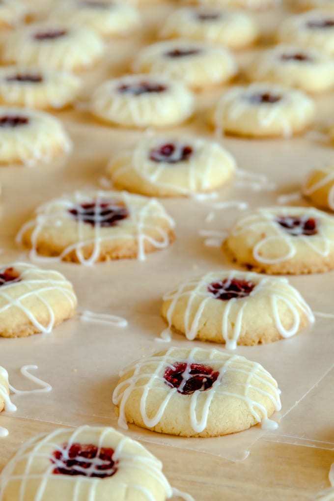 Close up image of thumbprint cookies drizzled with icing on parchment paper.