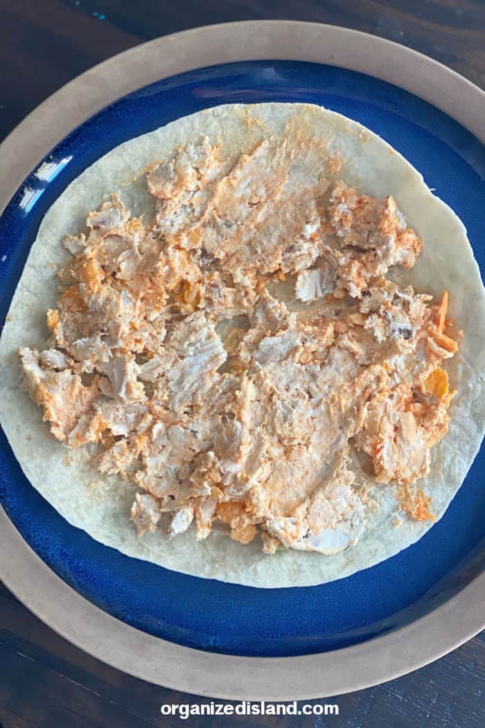 How To Make Buffalo Chicken Pinwheels: tortilla on plate and chicken mixture on tortilla.