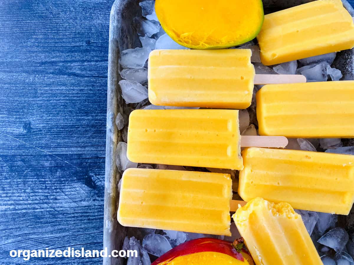 Easy Mango Popsicles on a tray with fresh mango.