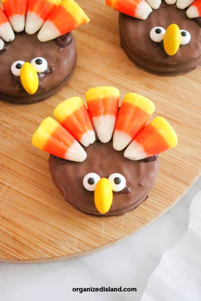 three decorated chocolate-covered oreo cookies decorated at turkeys with candy corn and eyes and a nose.