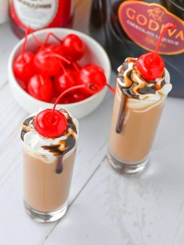 Chocolate Covered Cherry Shots with shipped cream and cherries on counter.