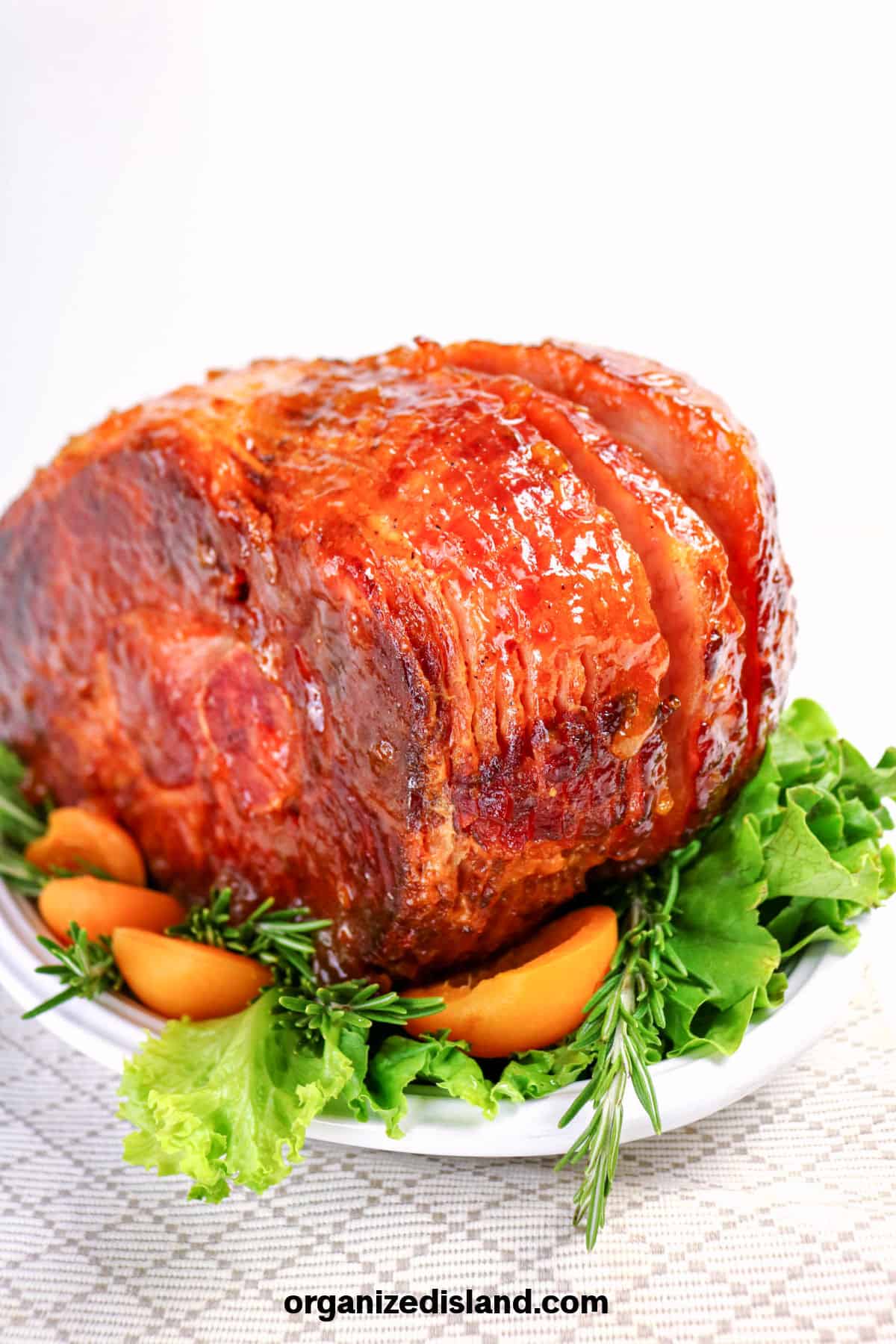 Juicy glazed ham on a white plate with fresh greens and orange slices.