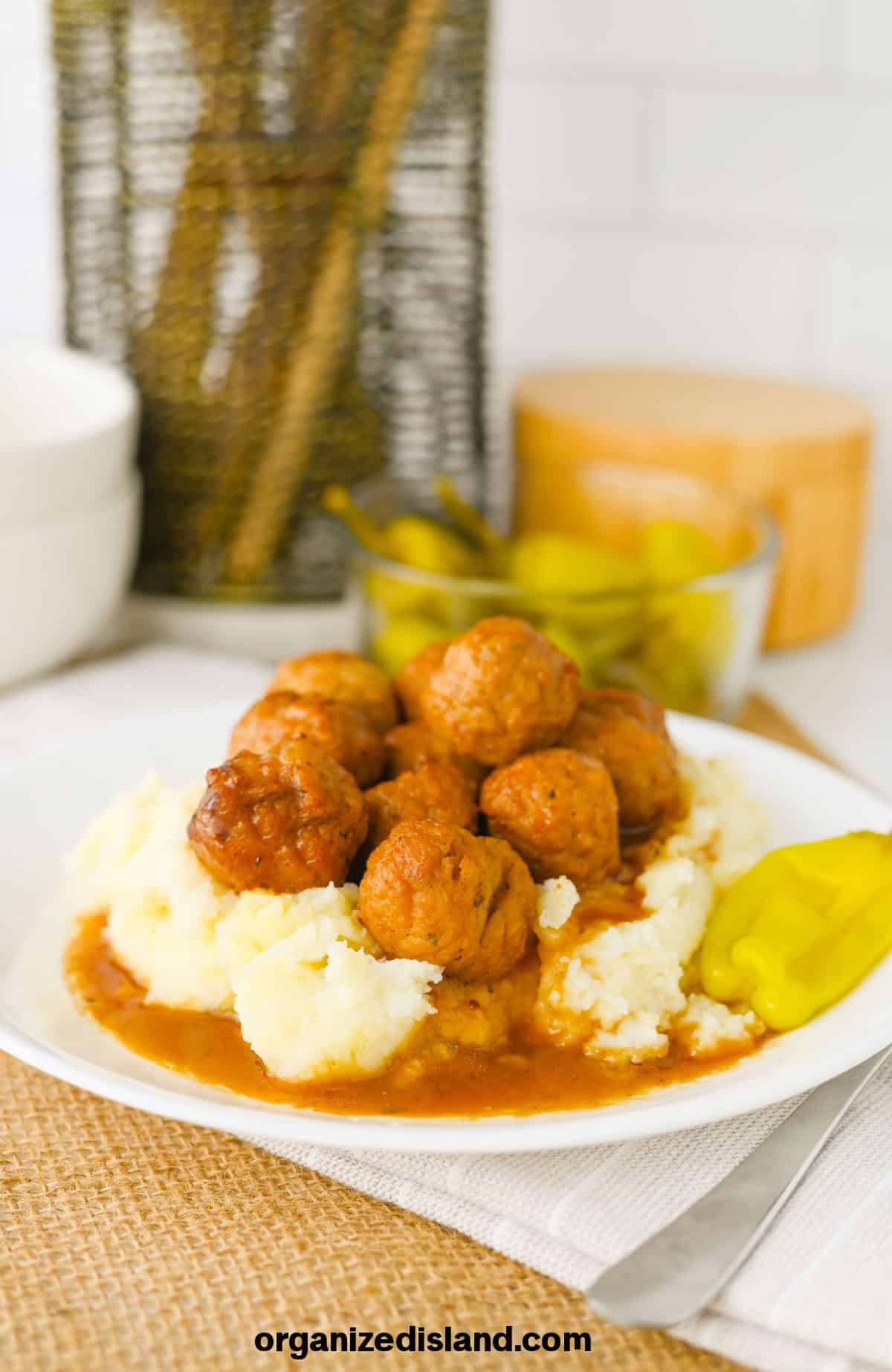 Delicious meatballs served over creamy mashed potatoes with gravy and a side of pickles, showcasing comfort food favorites.
