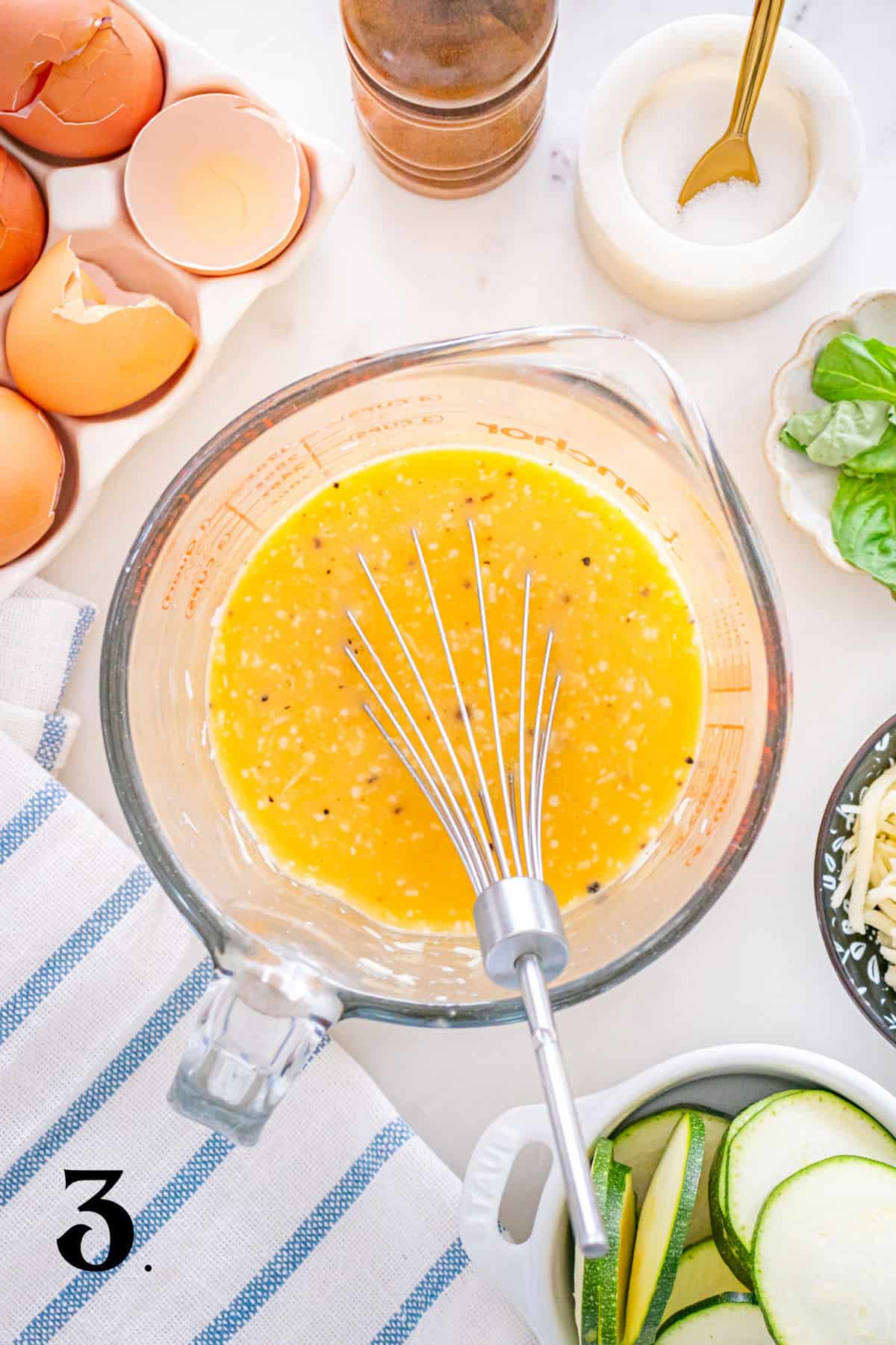 Egg mixture in a glass bowl with ingredients around it.
